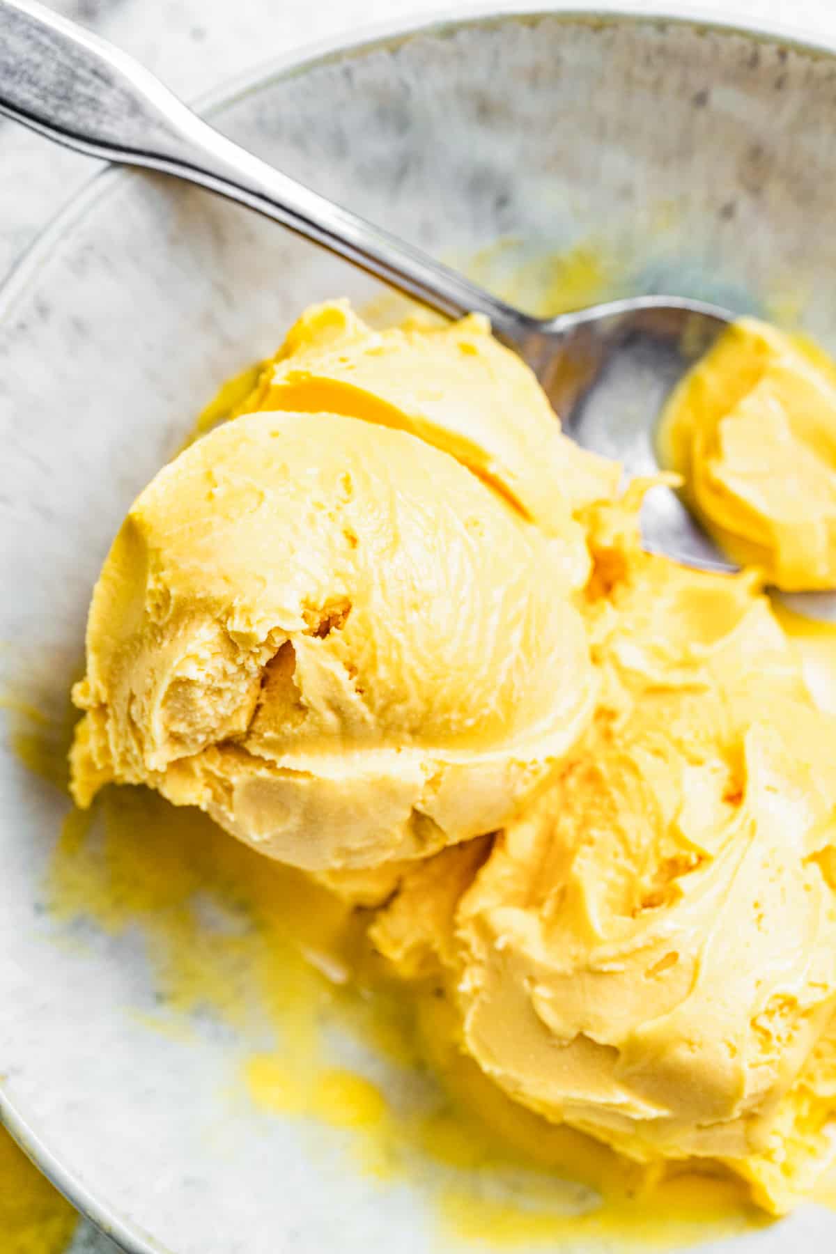 Two scoops of mango ice cream in a bowl with a spoon.