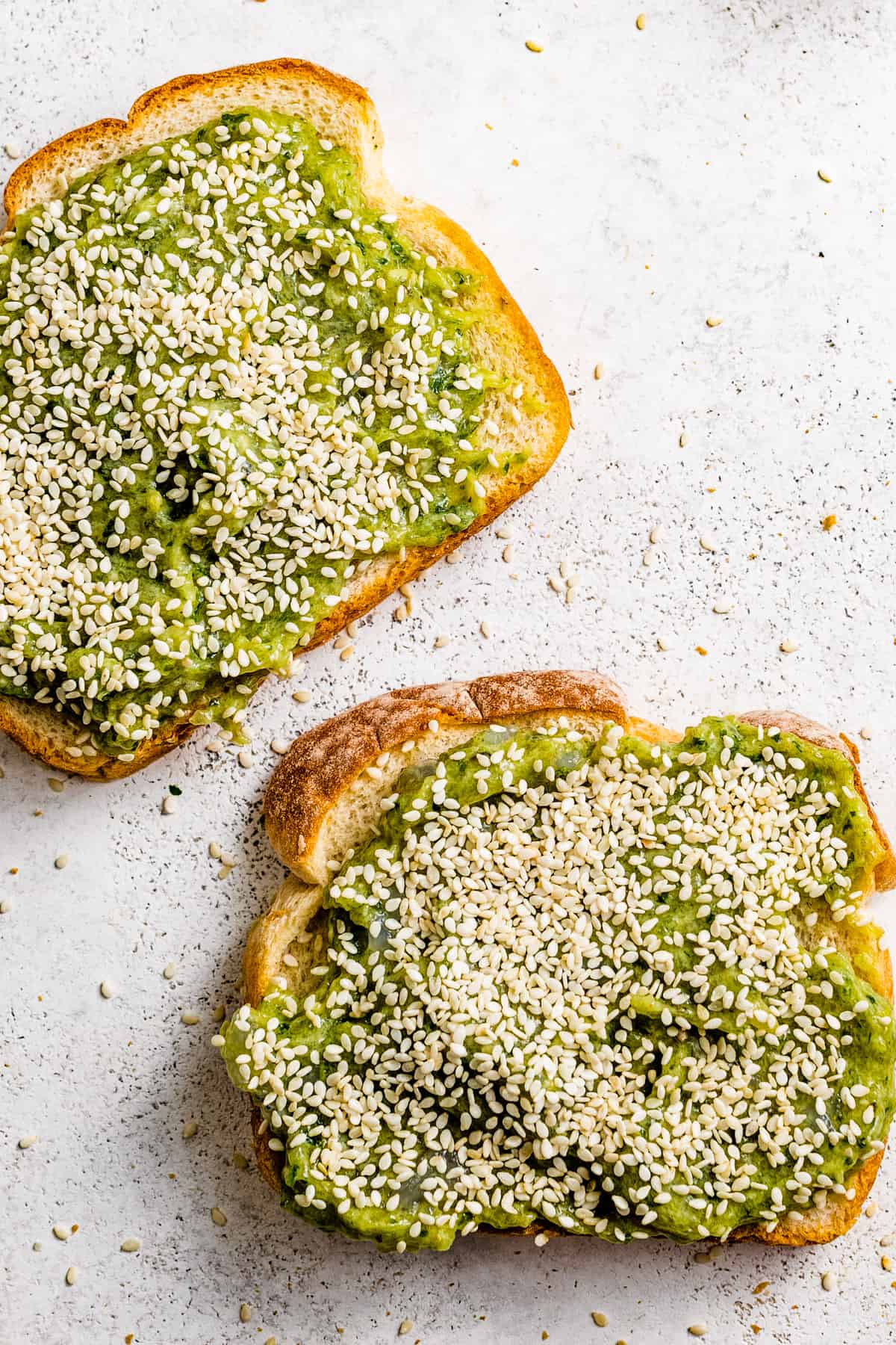 Two slices of sandwich bread topped with a green shrimp mixture and a layer of sesame seeds.