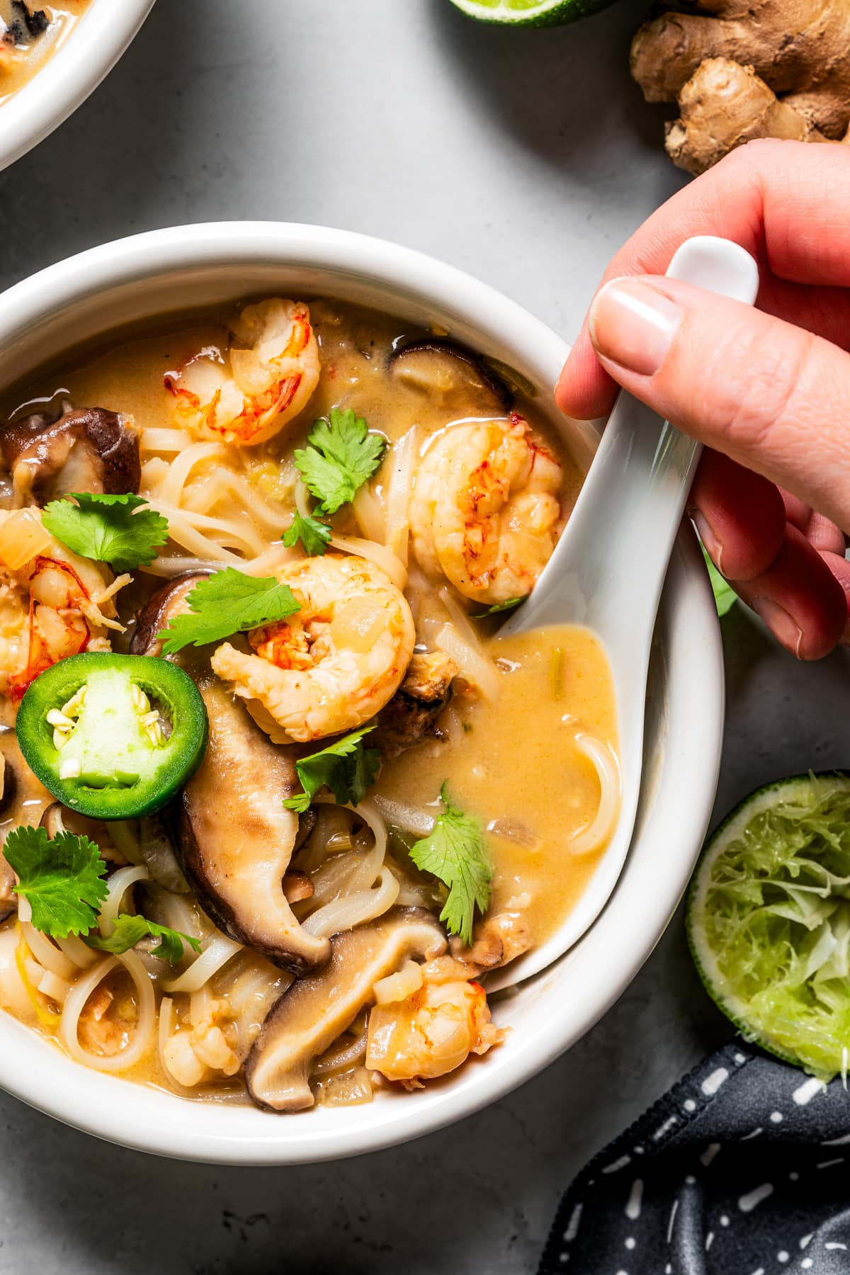 Spooning out a bite of tom yum soup in a bowl with a lotus spoon.