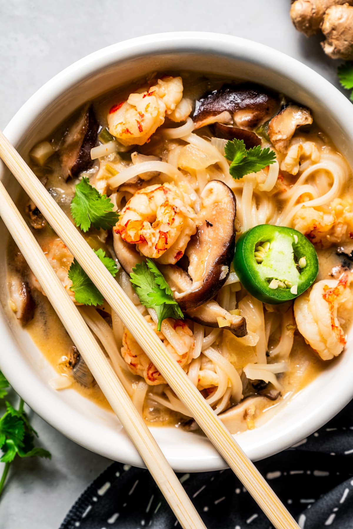 Tom yum noodle soup in a bowl garnished with herbs and a pair of chopsticks set on the bowl.