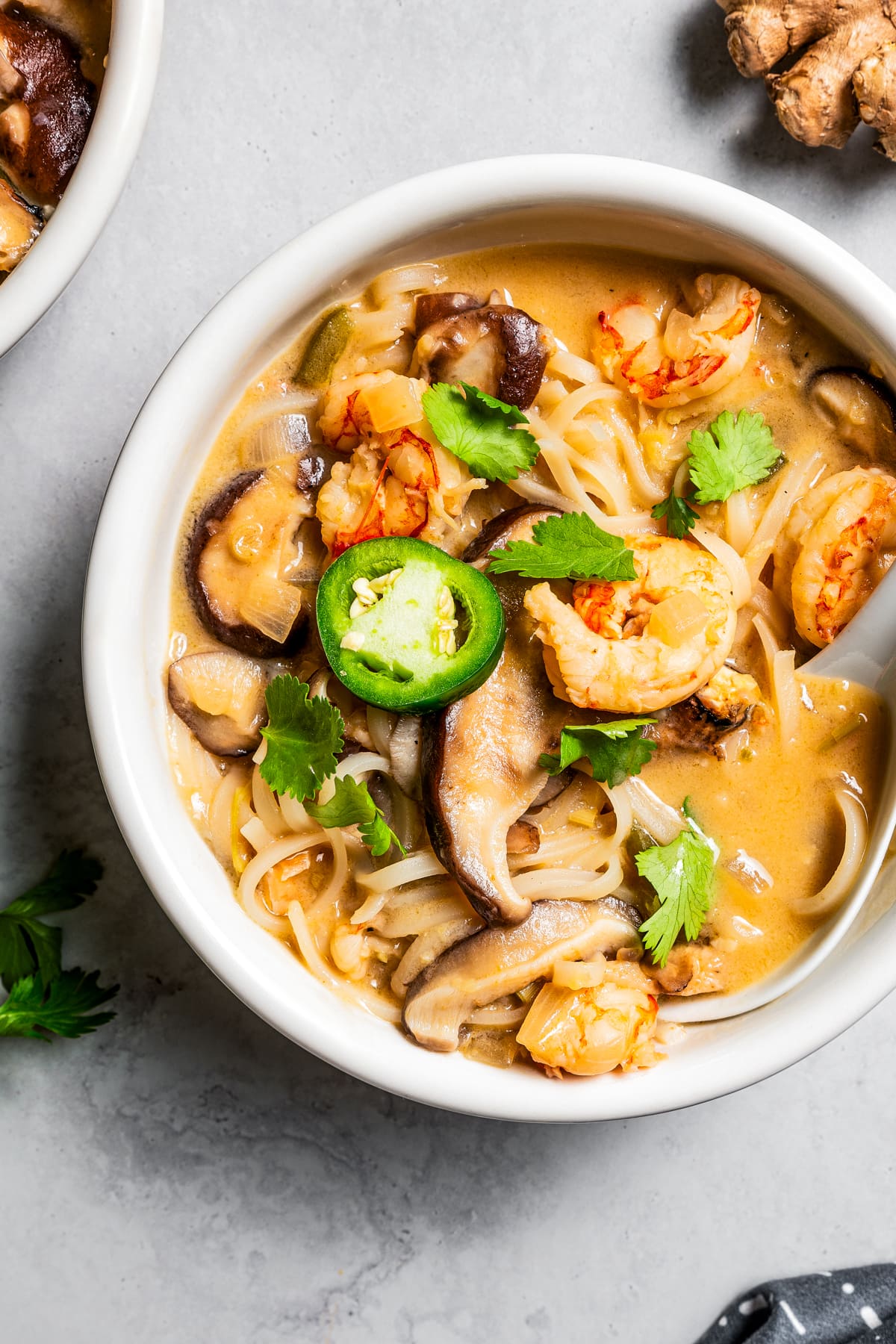 Overhead photo of tom yum noodle soup in a bowl, garnished with green peppers, herbs, and shrimp.