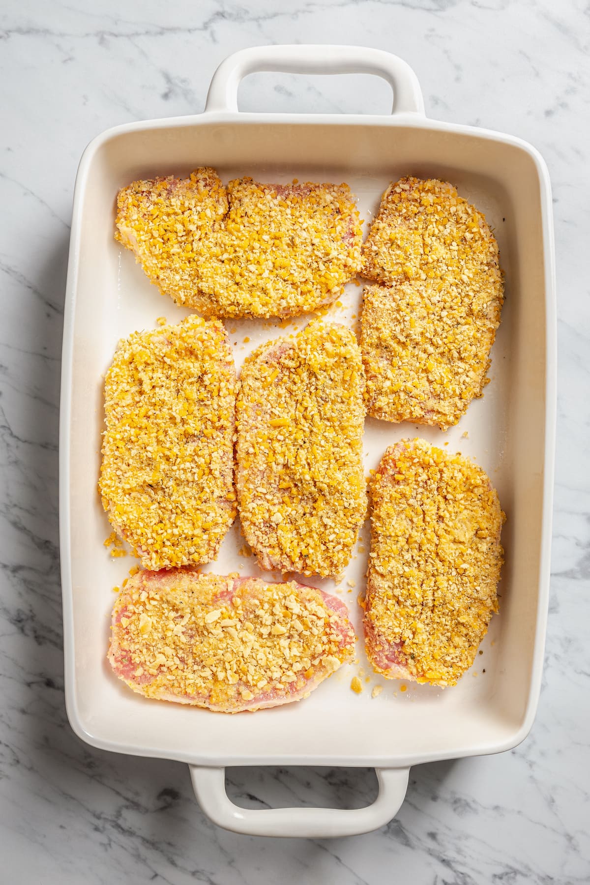 This crispy breaded pork chops recipe is an easy dinner, with juicy boneless pork chops coated in crunch and baked in the oven until golden. Breaded pork chops in a ceramic dish ready to be baked.