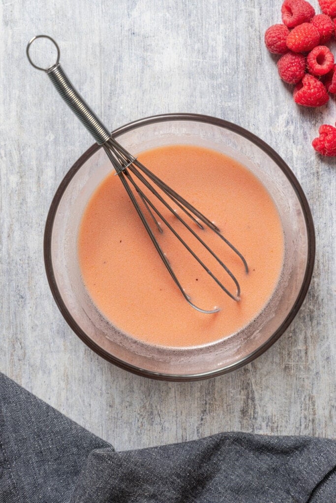 Raspberry vinaigrette in a mixing bowl with a whisk.