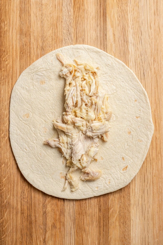 Wrapping chicken and cheese in a flour tortilla.