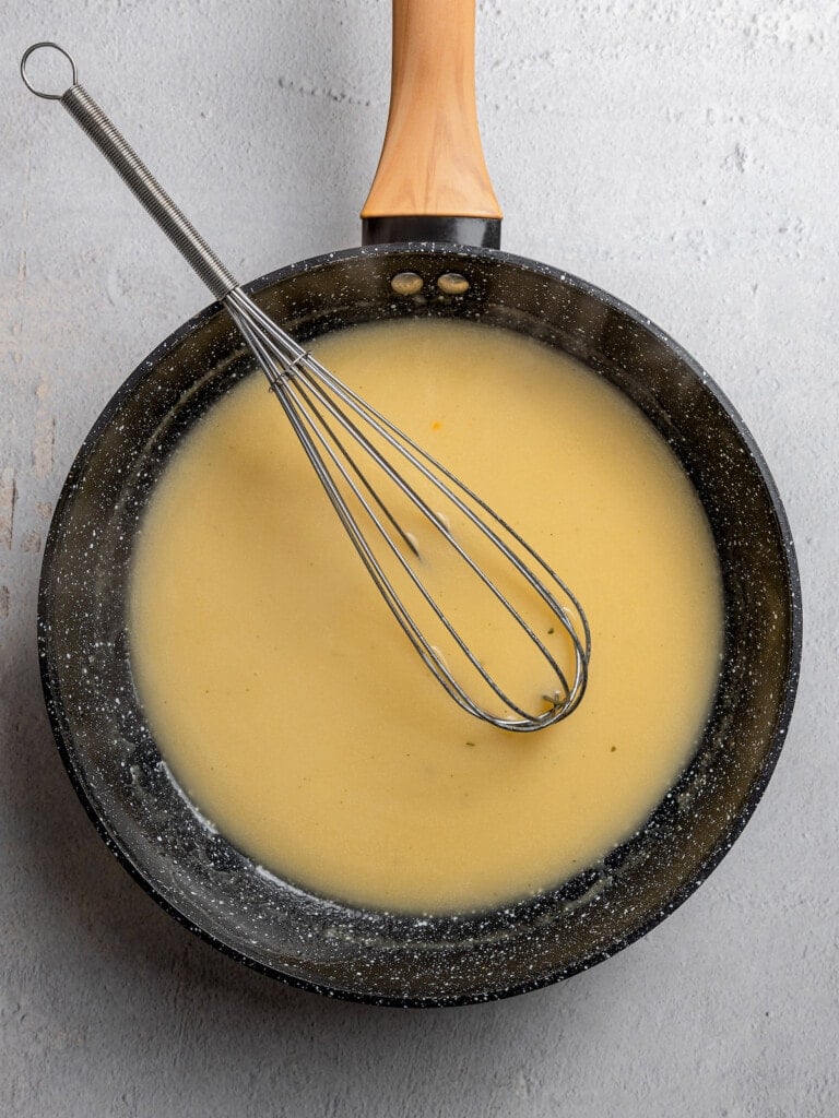 Whisking chicken stock into a roux to make a sauce.