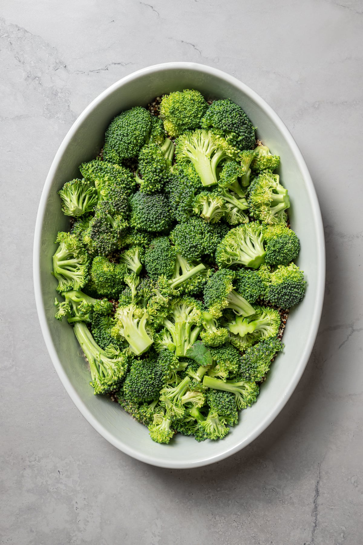 Adding broccoli to a layer of quinoa in a casserole dish.