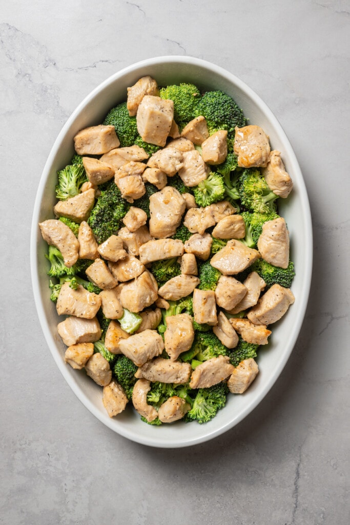 Adding browned chicken to a layer of broccoli in a casserole dish.