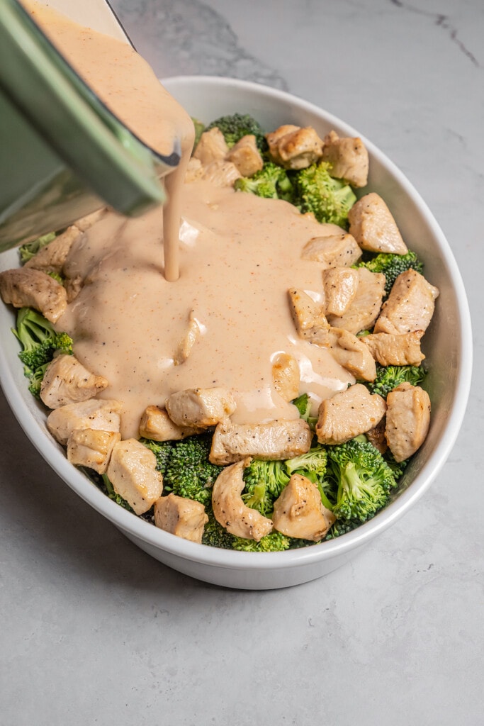 Pouring sauce over chicken and broccoli casserole.