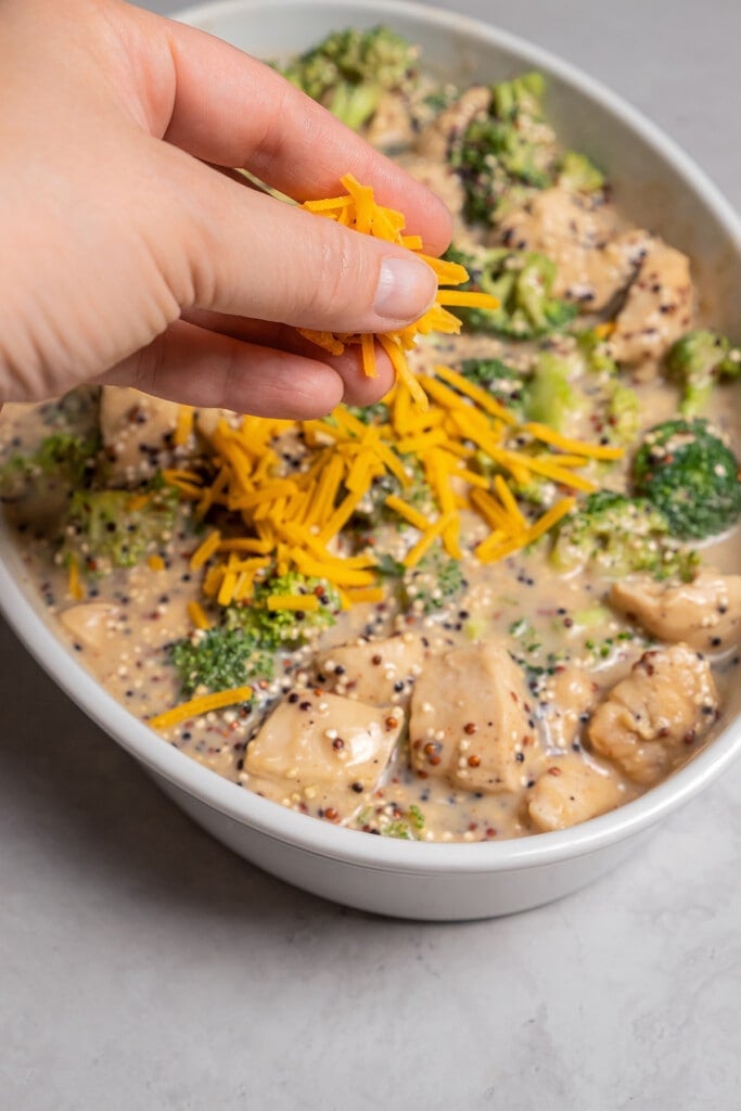 Sprinkling cheese over chicken and broccoli casserole.
