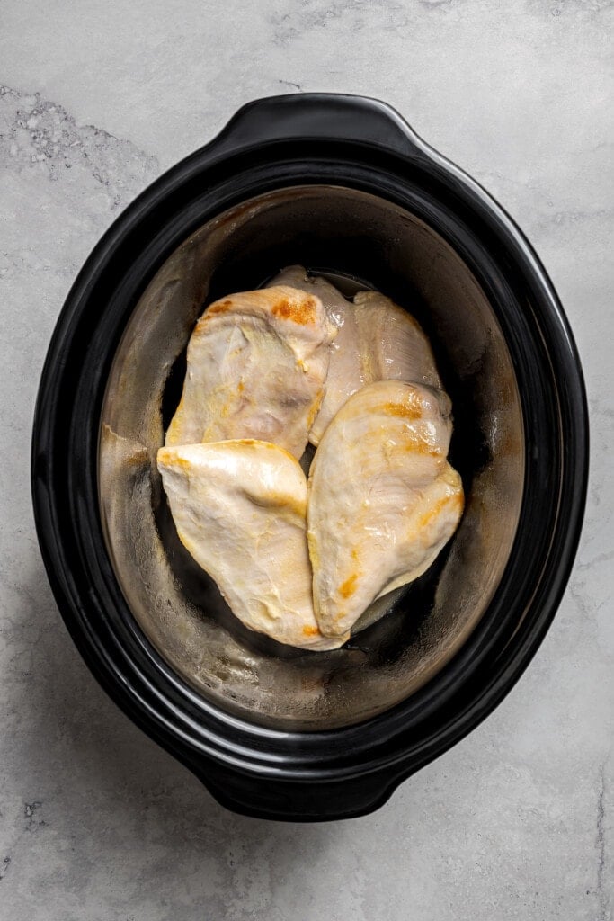Putting browned chicken thighs in a crockpot.
