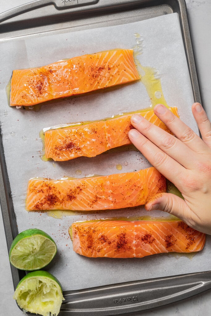 Rubbing chili powder into raw fillets of salmon on a baking sheet lined with parchment paper.
