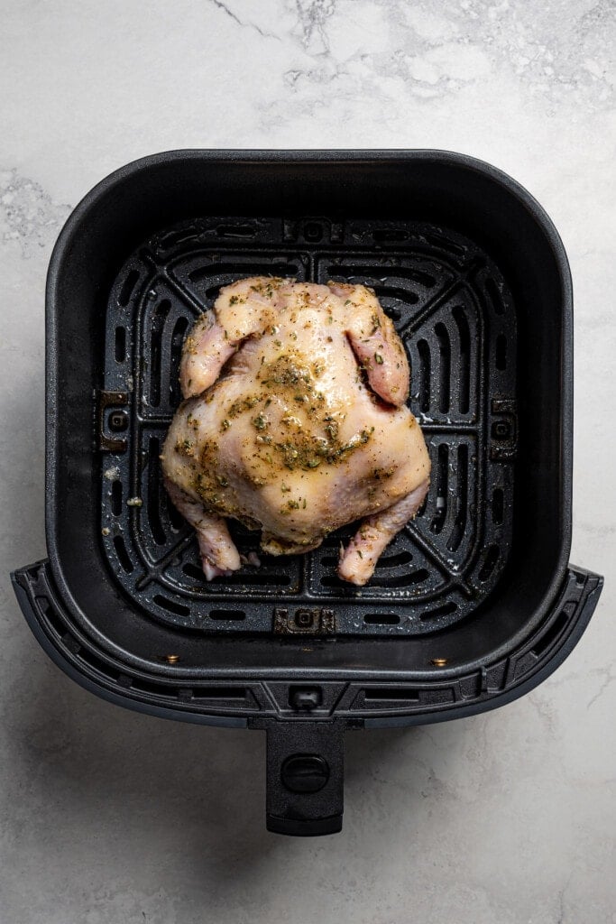 Placing seasoned cornish game hen breast side down in the basket of an air fryer.