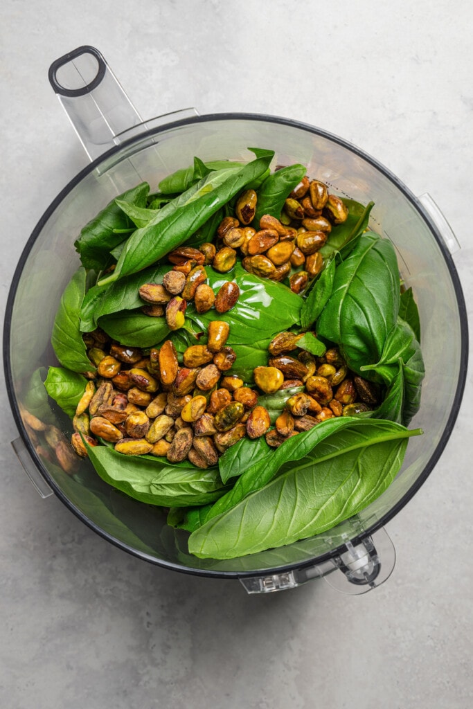 Combining fresh basil leaves, olive oil, and pistachios in a food processor.