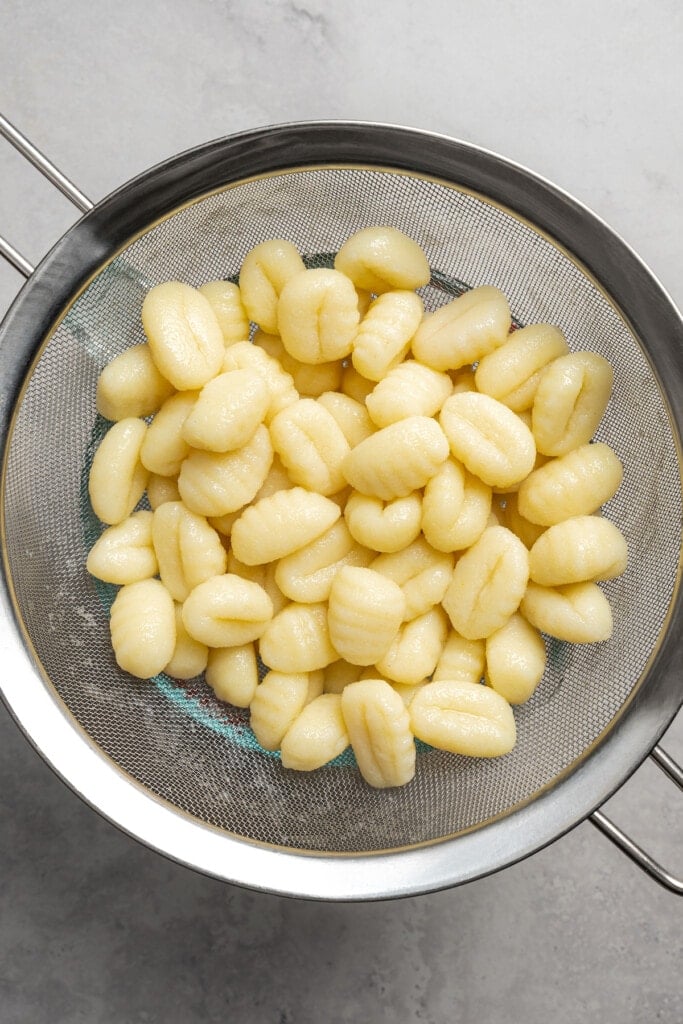 Draining cooked gnocchi.