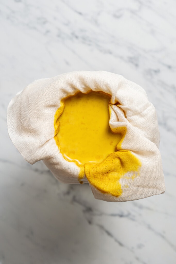 Overhead shot of straining golden latte through a cheesecloth into a mason jar.