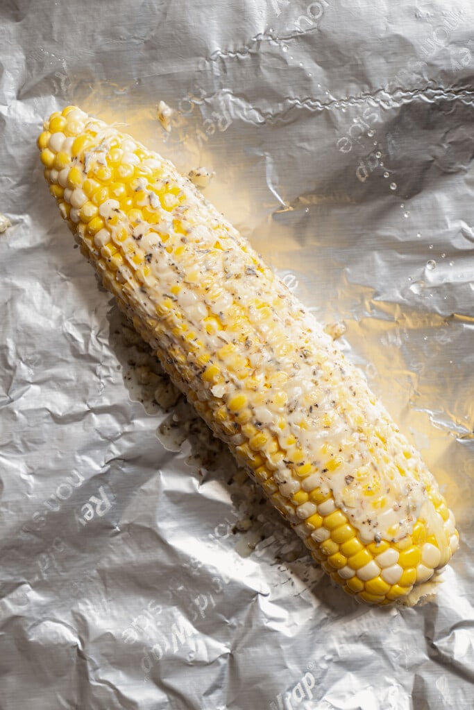 Corn on the cob covered with herb butter on a sheet of foil.