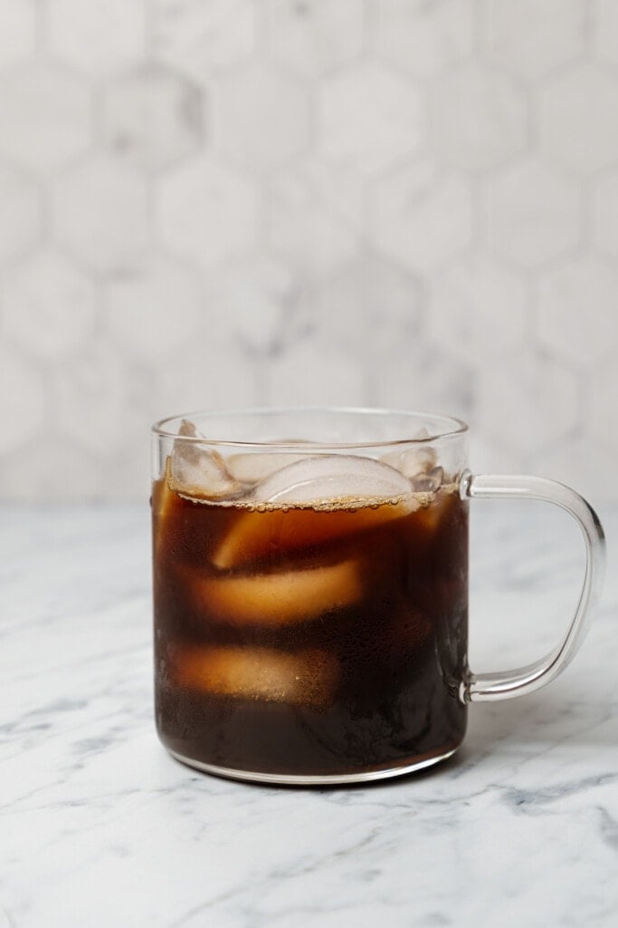 Iced Americano in a glass coffee mug on a white marble countertop.