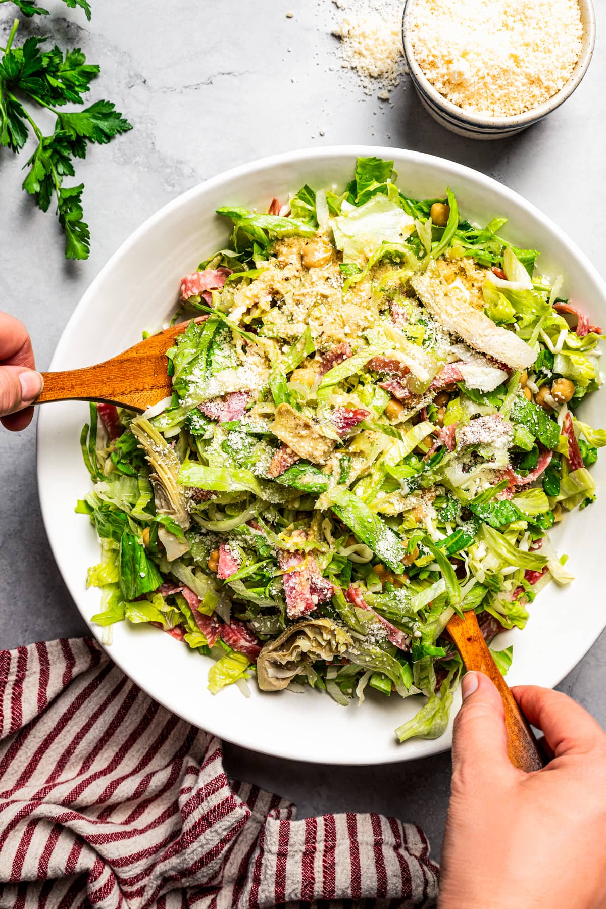 Hands using two wooden salad scoops to toss a La Scala chopped salad in a large serving bowl.