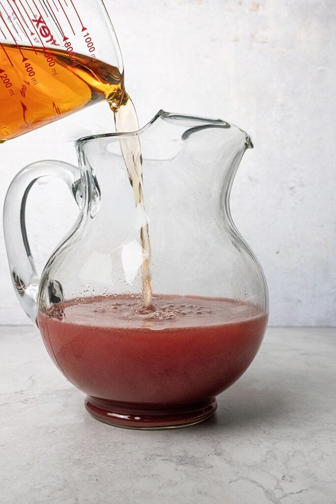 Side view of white grape juice being added to the strawberry acai refresher base in a pitcher.