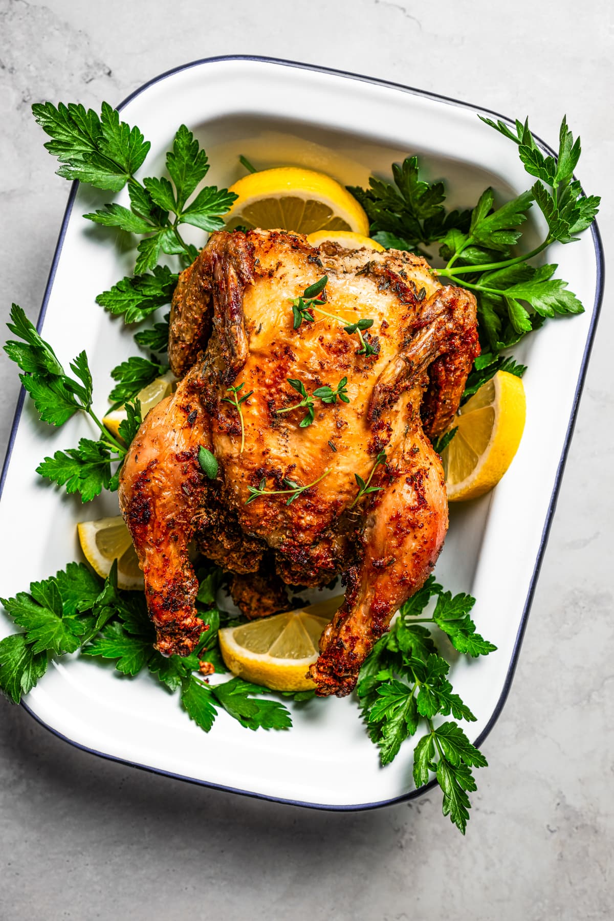 Overhead image of air fryer cornish game hen on a bed of fresh parsley. A fork and knife are at the ready nearby.