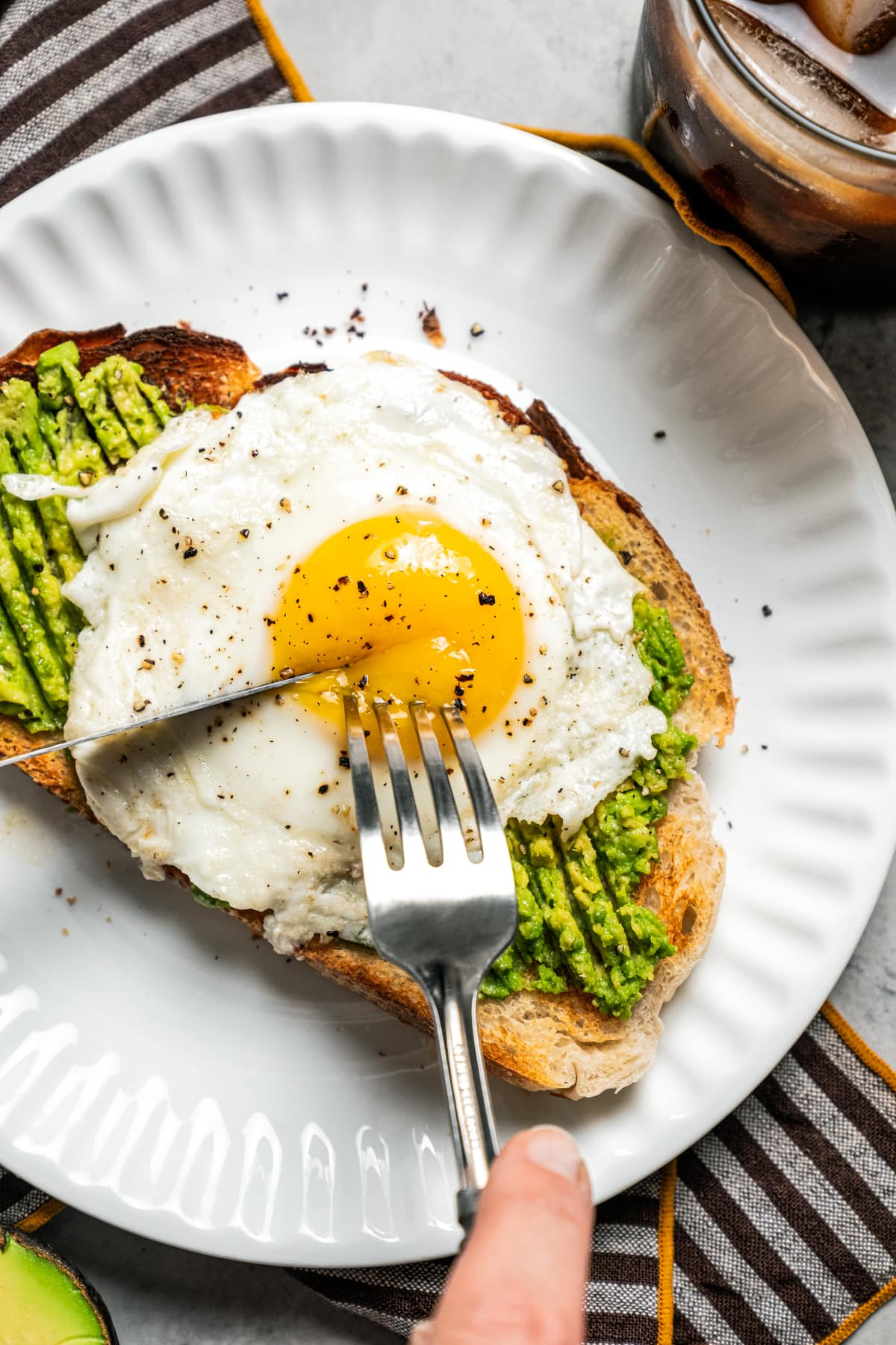 Using a fork and knife to cut into avocado toast with egg on top.