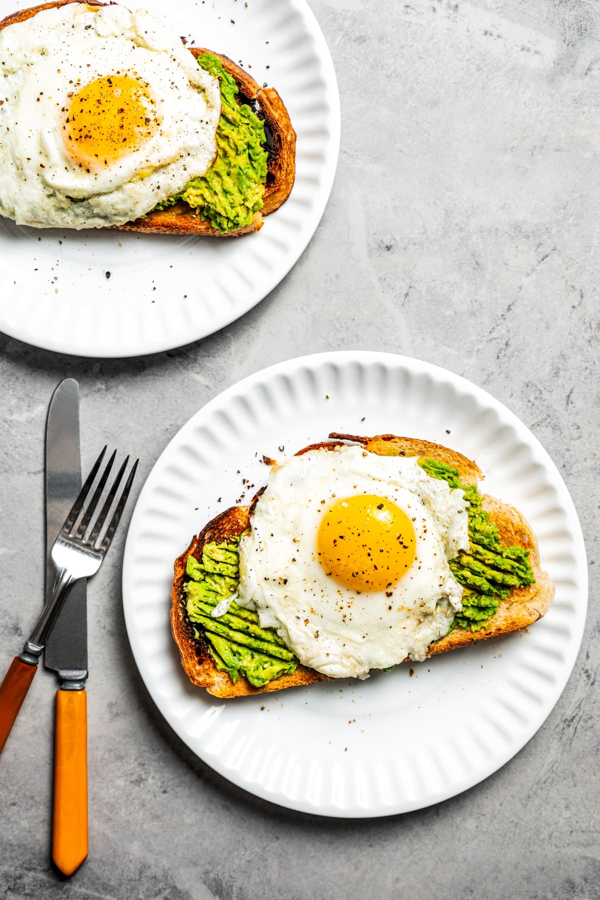 Two white plates holding Avocado toasts topped with a sunny side-up egg.