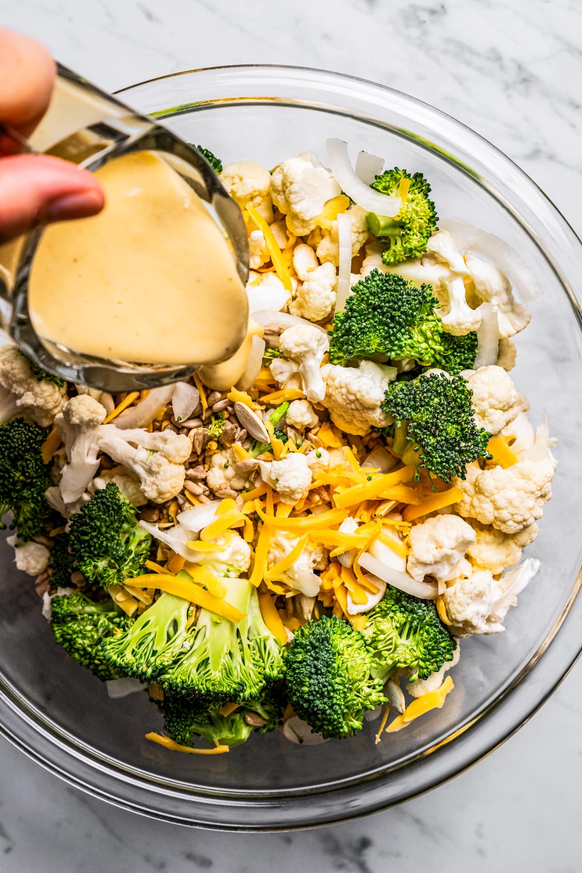 Pouring dressing over broccoli cauliflower salad.