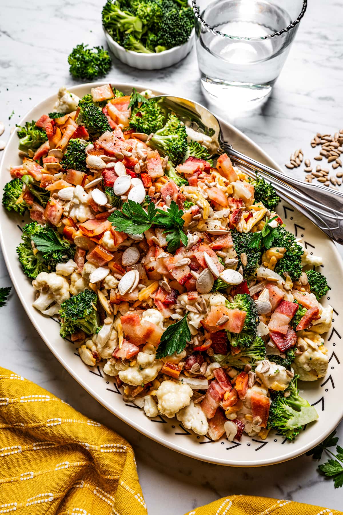 Broccoli cauliflower salad on a serving plate with a serving spoon near a glass of water.