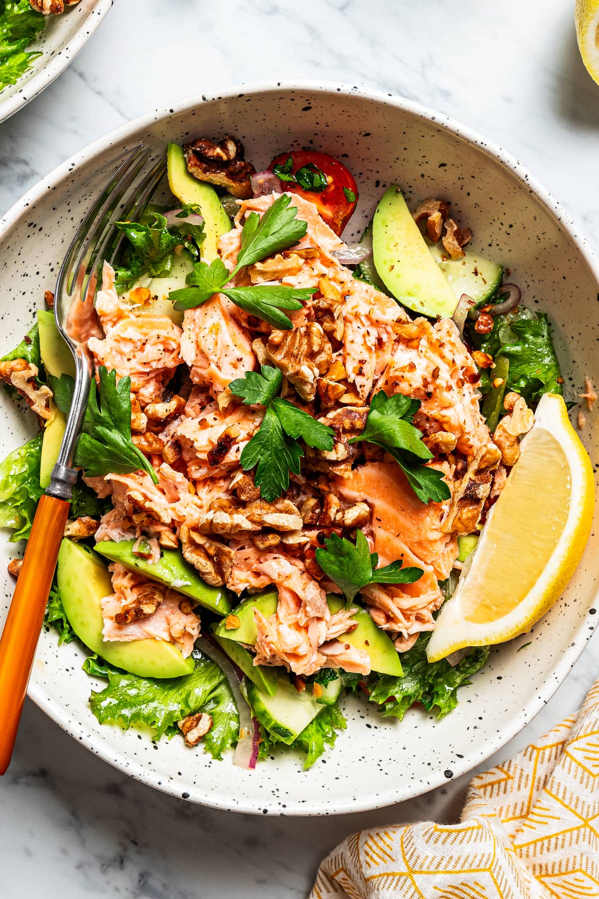 Close-up of a salmon salad in a bowl with salad greens, tomatoes, and a wedge of lemon.