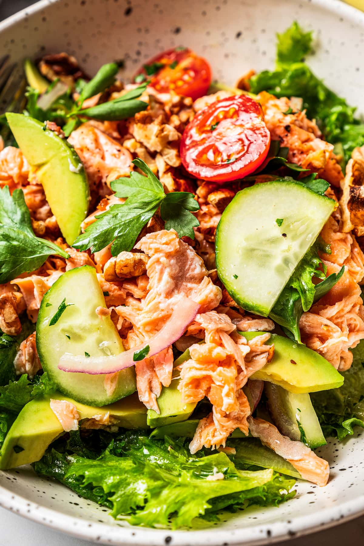 Close-up of chopped salmon salad in a bowl with salad greens and tomatoes.