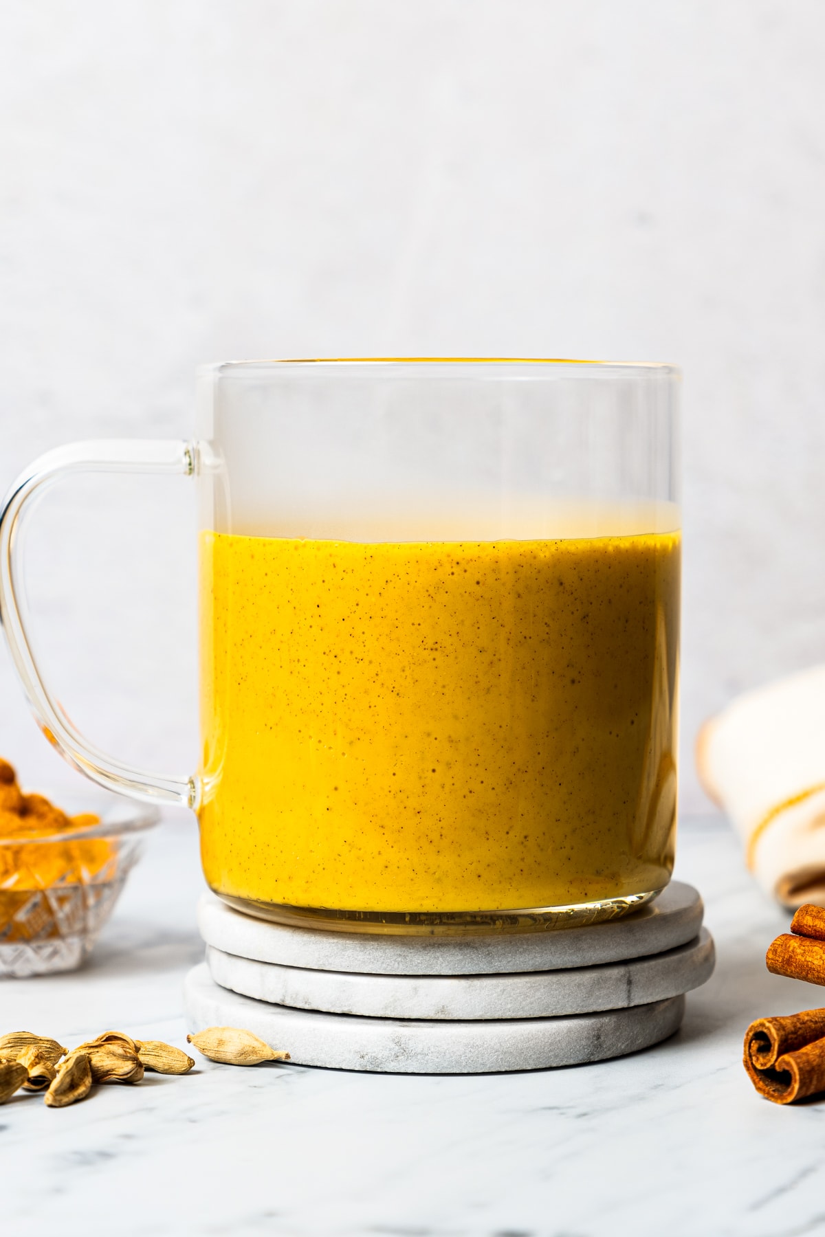 Close-up of a glass mug filled with turmeric latte near a bowl of turmeric and other whole spices.