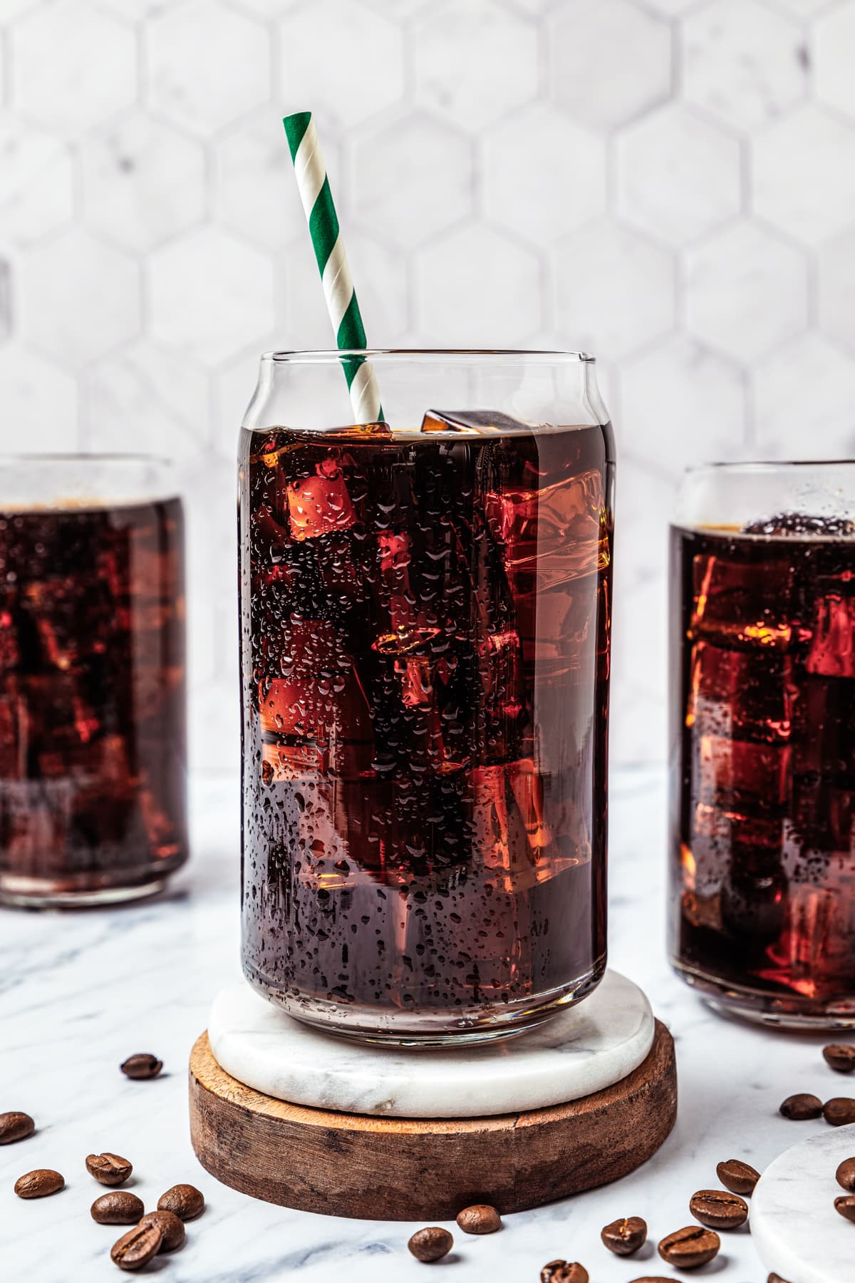 Close-up of iced Americano drinks on a coaster, with two more glasses with iced coffee set behind it.