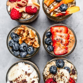 Top view of six mason jars with protein oatmeal and topped with various fruits.