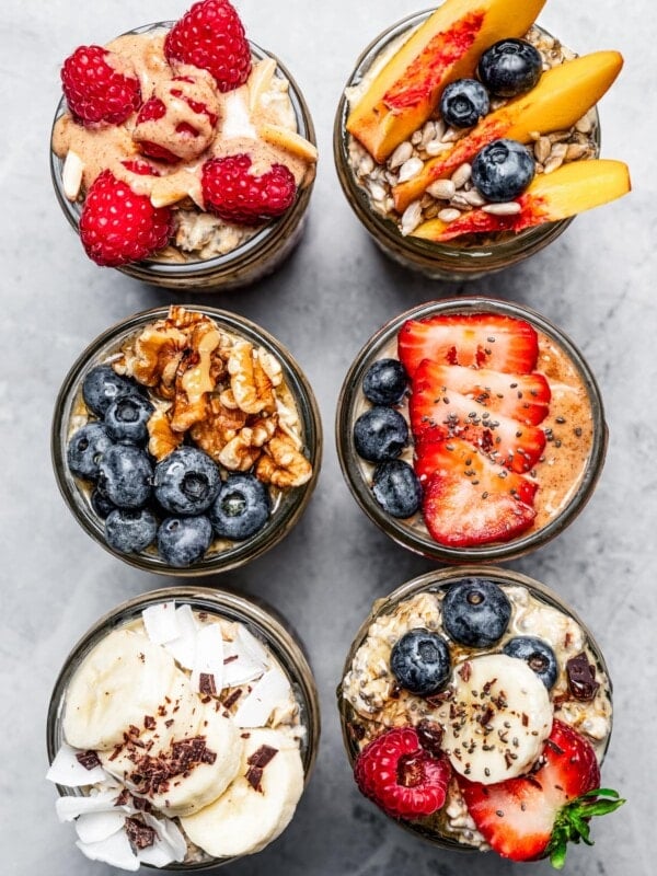 Top view of six mason jars with protein oatmeal and topped with various fruits.