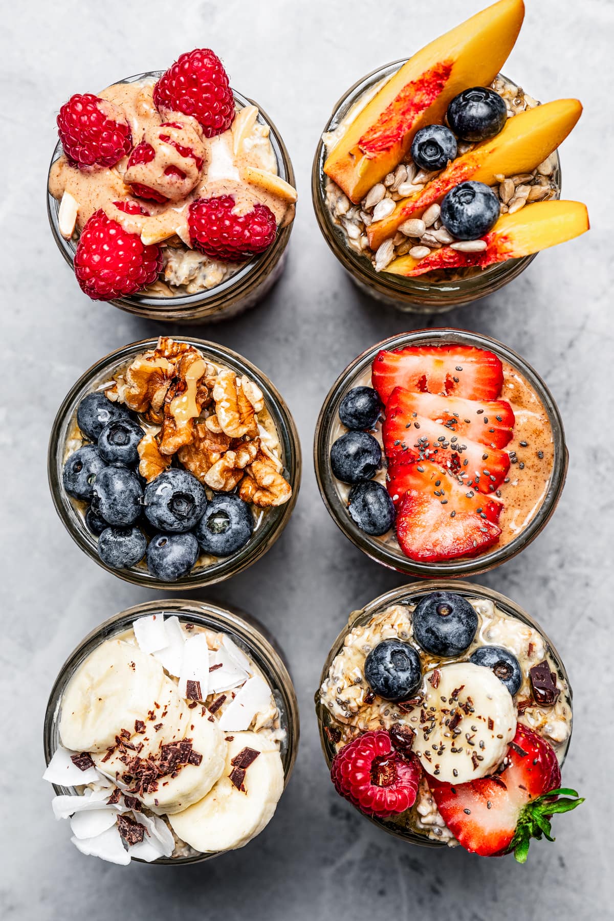 Top view of six mason jars with protein oatmeal, each topped with various fruits and nuts.