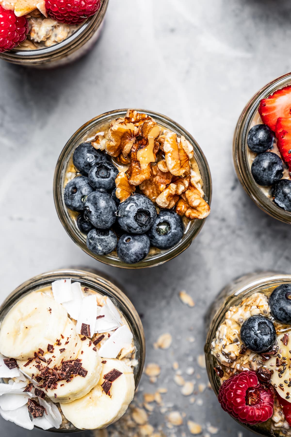Overhead image of protein oatmeal in jars topped with blueberries, bananas, walnuts, and strawberries.