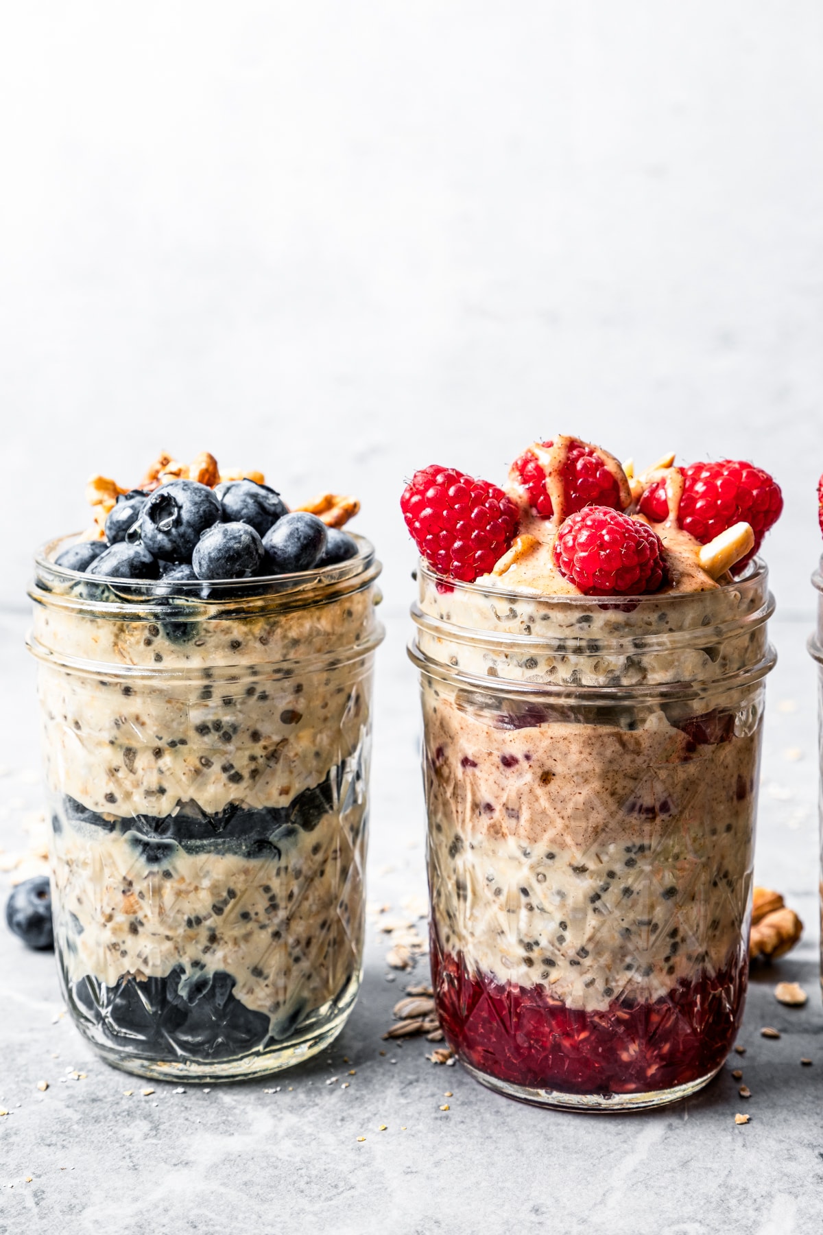 Side view of two mason jars filled with oatmeal and topped with berries and nuts.