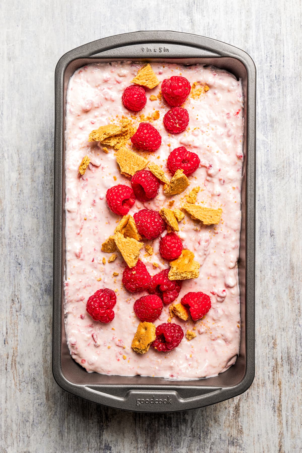Raspberry cottage cheese ice cream in a loaf pan with raspberries and graham crackers on top.