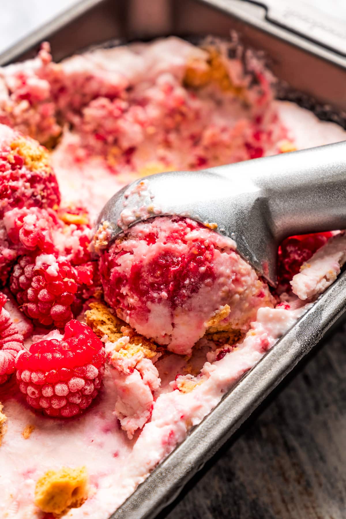 Closeup shot of scooping raspberry cottage cheese ice cream out of a loaf pan.