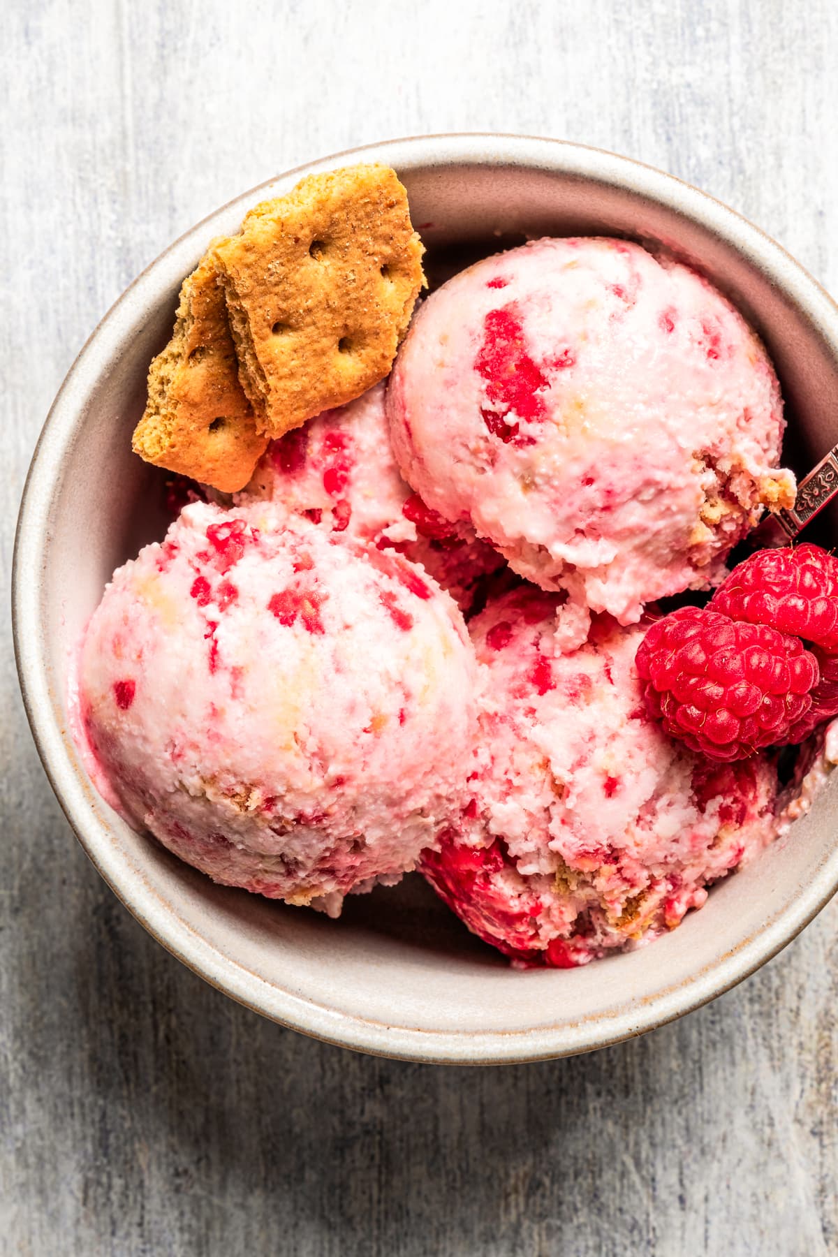 Overhead image of raspberry cottage cheese ice cream served in a bowl and garnished with fresh raspberries and graham crackers.