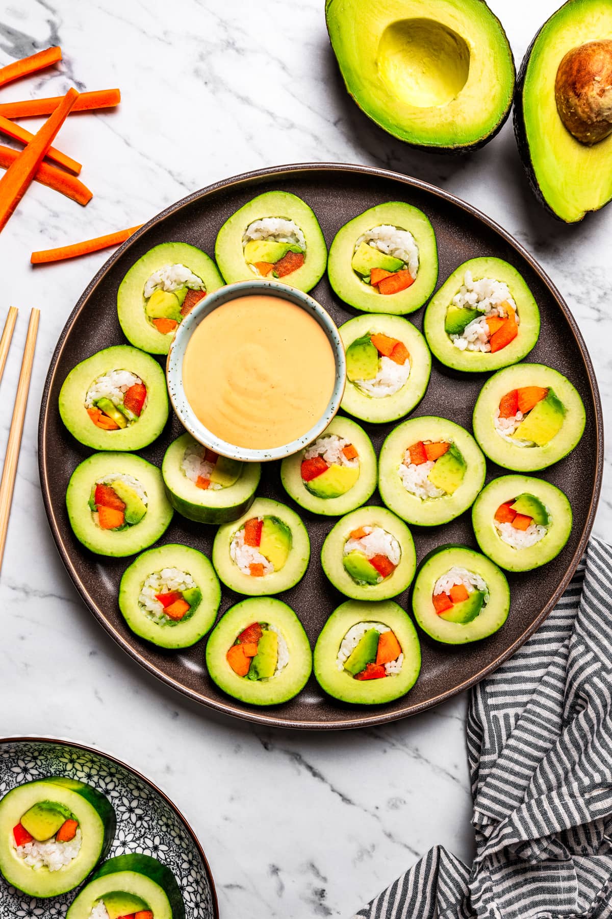 A platter loaded with sliced cucumber rolls and sriracha dipping sauce.