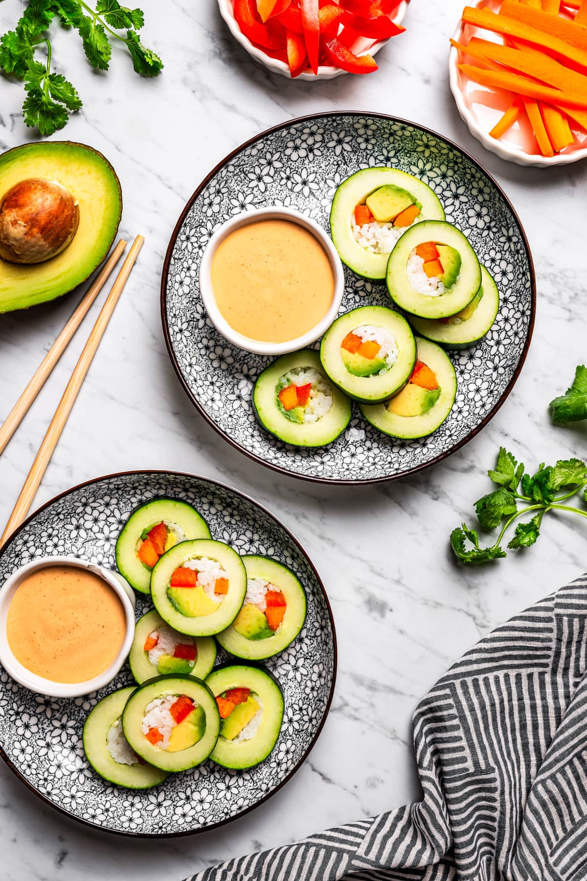 Overhead image of two plates loaded with sliced cucumber rolls with sriracha dipping sauce.