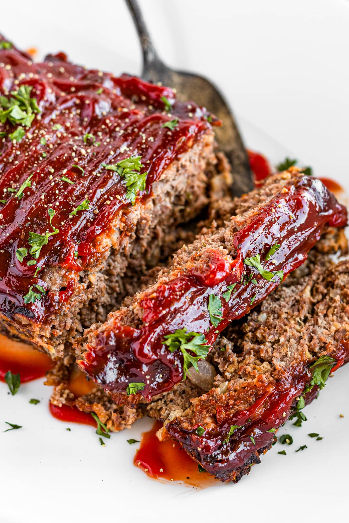 Meatloaf topped with red sauce and parsley, and sliced.