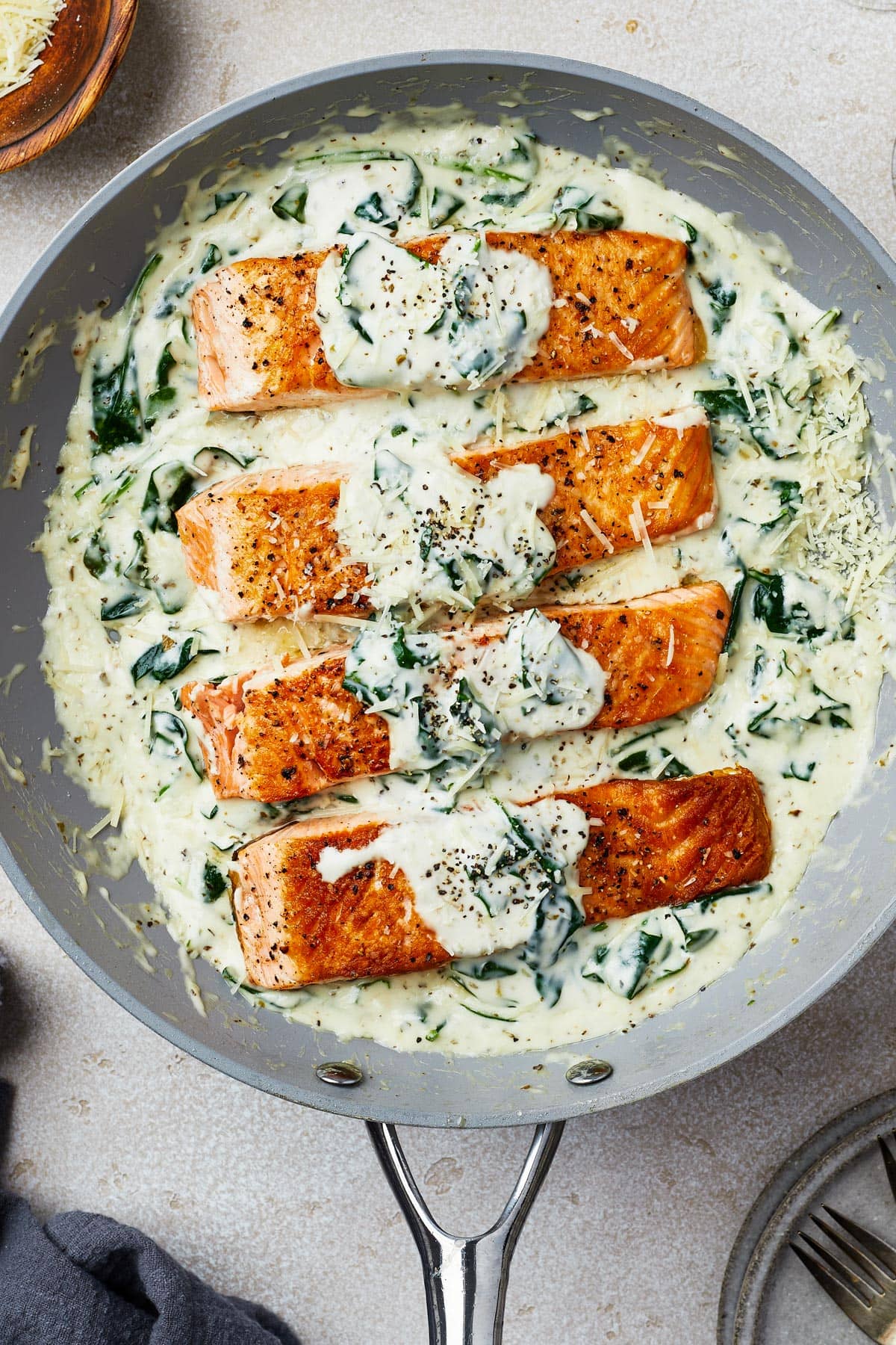 Overhead shot of a skillet with four salmon fillets topped with a creamy spinach sauce.