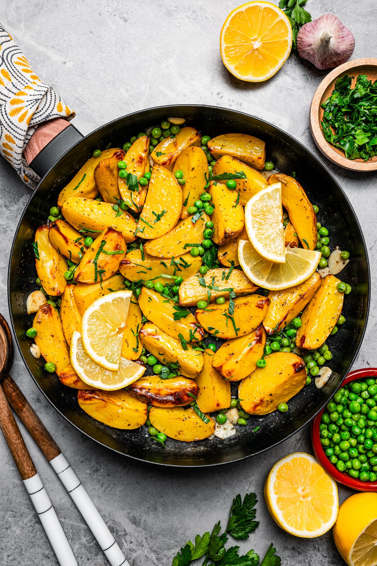 Vesuvio potatoes in a skillet surrounded by lemons, parsley, and peas.