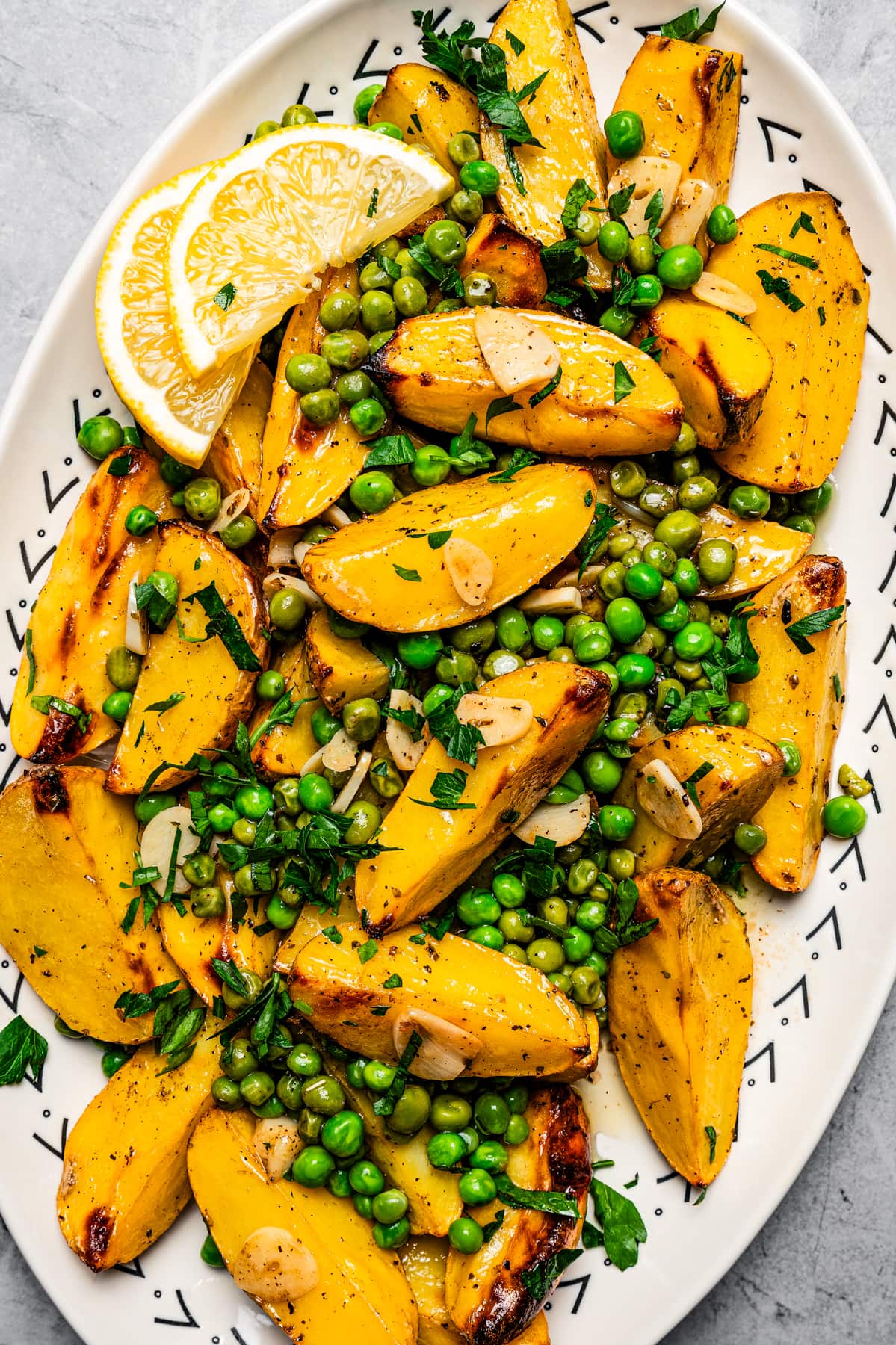 Overhead image of Vesuvio potatoes on a serving platter with lemon slices and serving spoons.