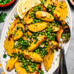 Overhead image of Vesuvio potatoes on a serving platter with lemon slices and serving spoons.