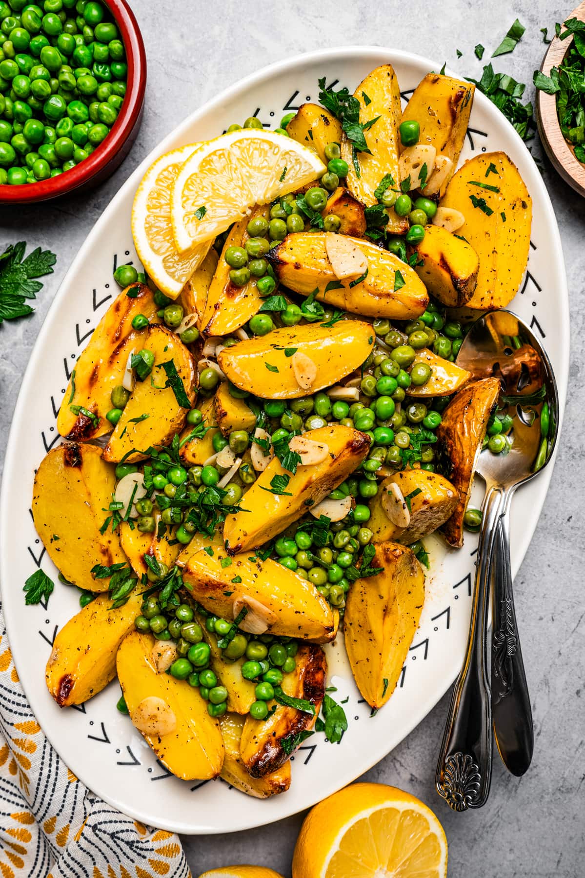 Overhead image of Vesuvio potatoes on a serving platter with lemon slices and serving spoons.
