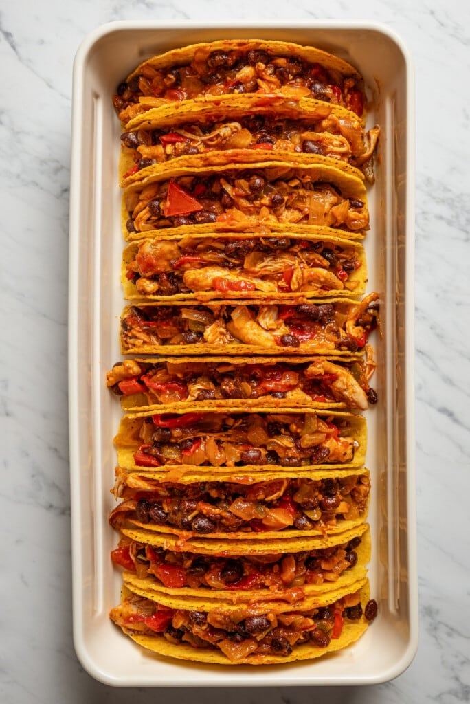 Filling taco shells with shredded chicken and black beans filling.