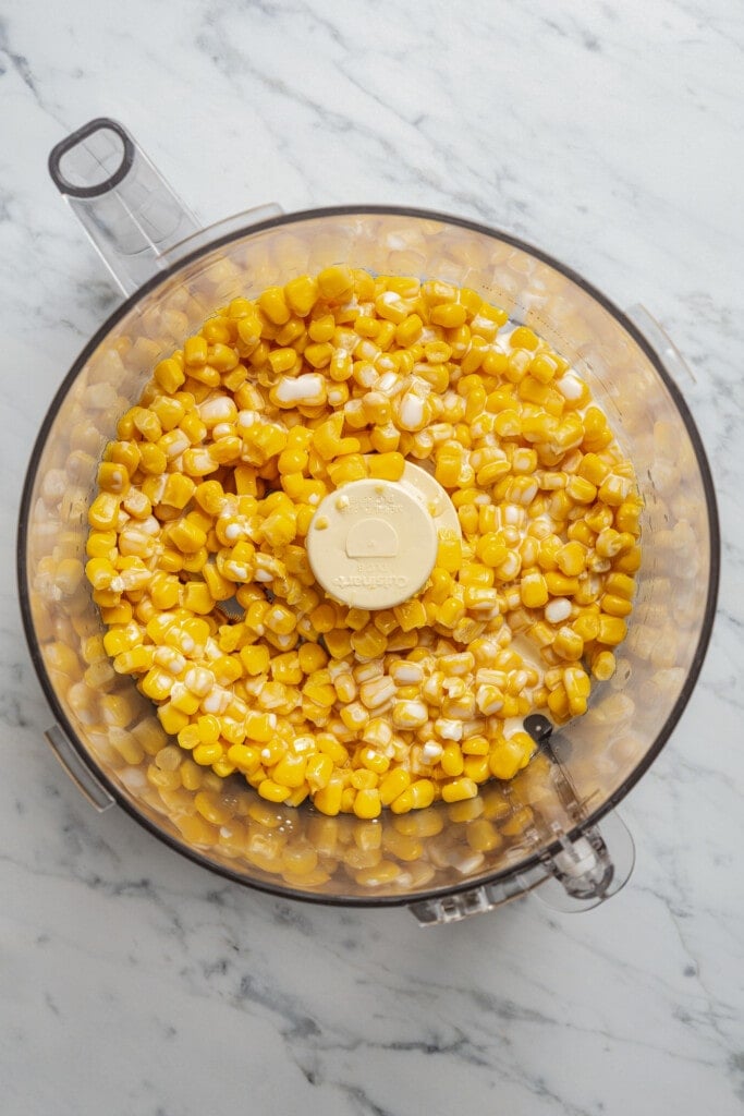Adding heavy cream and corn kernels to a food processor.